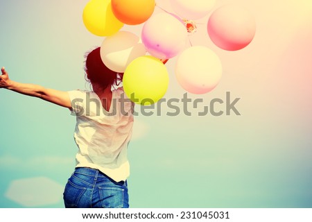 young asian woman running and jumping on green grassland with colored balloons 