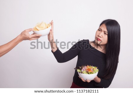 Young Asian woman with salad say no to potato chips on white background