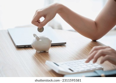 Young Asian woman saving for retirement Saving money through a piggy bank and taking notes on notebook, savings concept. - Shutterstock ID 2311595581
