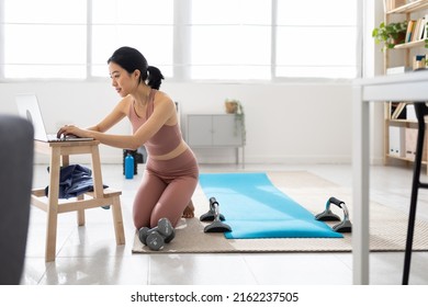 Young Asian Woman Searching For Virtual Fitness Class On Laptop At Home