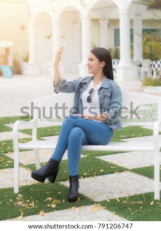 Young Asian woman selfie on smartphone sitting on white chair in the garden