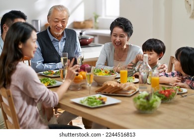 young asian woman sharing pictures in cellphone with three generation family while eating meal together - Powered by Shutterstock