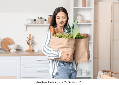 Young Asian woman with shopping bags full of fresh food in kitchen