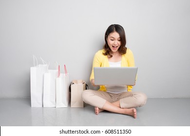 Young Asian Woman Shopping Online At Home Sitting Besides Row Of Shopping Bags