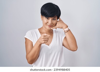 Young asian woman with short hair standing over isolated background smiling doing talking on the telephone gesture and pointing to you. call me.  - Powered by Shutterstock