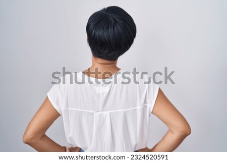 Young asian woman with short hair standing over isolated background standing backwards looking away with arms on body 