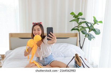 Young Asian Woman Show Yellow	Bikini While Talking To Facetime Calling With Her Friend In Bedroom. Using Smartphone Taking Selfie On Front Camera 