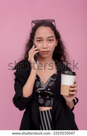 A young asian woman sighs while having a stressful conversation over the phone while holding a cup of coffee. Isolated on a light pink background. Mobile phone advertisement layout.