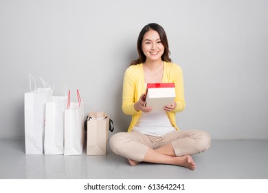 Young Asian Woman Sitting Besides Row Of Shopping Bags Holding Red Gift Box