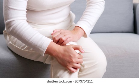 Young Asian Woman Sitting On Sofa Performing Self Knee Massage  Concept Of Self Physiotherapy Due To Knee Pain 