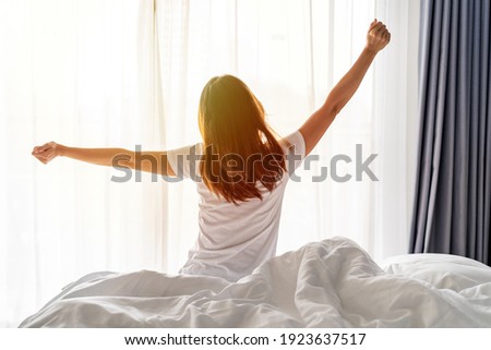 Young asian woman sitting on the bed and stretch oneself in the morning at home