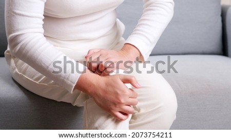 Young Asian woman sitting on sofa performing self knee massage  Concept of self physiotherapy due to knee pain 