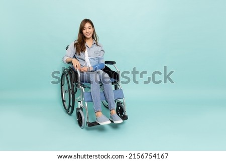 Young Asian woman sitting on wheelchair and put on a soft splint due to a broken arm isolated on green background, Personal accident concept