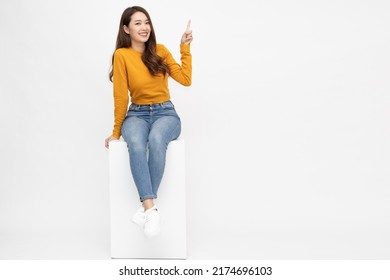 Young Asian woman sitting and pointing to empty copy space isolated on white background, Full body composition - Shutterstock ID 2174696103