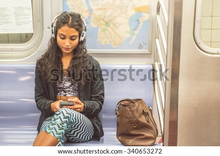 Young asian woman sitting in a subway car and listening music with her smartphone - Pretty girl riding on a train and going to work