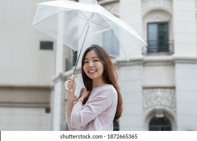 Young Asian Woman Smile And Holding A Transparent Umbrella Under The Rain In The City