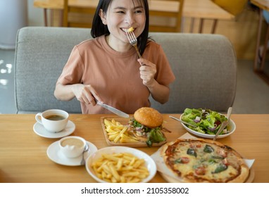 Young Asian woman smiling with her food, pizza, hamburger, A woman holding fork and steak knife feeling happy and enjoy to eat food in the restaurant. Enjoy eating concept. Italian food.