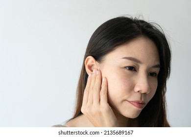 Young Asian woman with sore ear suffering from otitis over white background. Girl touch her ear with pain. Ear problem, health concept. Copy space, closeup