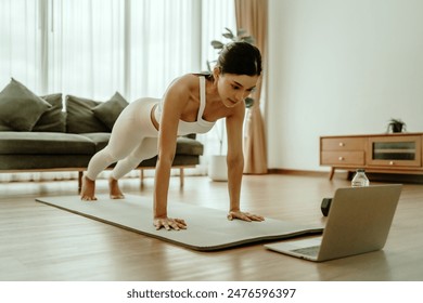 Young Asian woman in sportswear doing plank on training mat while watching online workout tutorials on laptop in the living room. Sport and recreation concept - Powered by Shutterstock