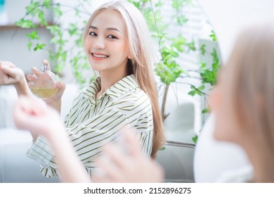 Young Asian Woman Spraying Perfume In Front Of Mirror
