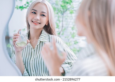 Young Asian Woman Spraying Perfume In Front Of Mirror
