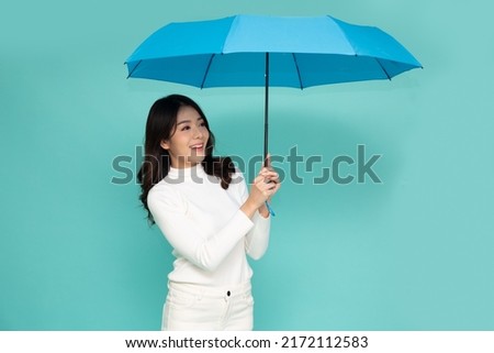 Young Asian woman standing and holding blue umbrella isolated on green background, In the rainy season concept