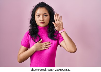 Young Asian Woman Standing Over Pink Background Swearing With Hand On Chest And Open Palm, Making A Loyalty Promise Oath 