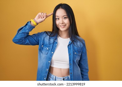 Young Asian Woman Standing Over Yellow Background Smiling Pointing To Head With One Finger, Great Idea Or Thought, Good Memory 