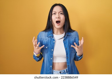 Young asian woman standing over yellow background crazy and mad shouting and yelling with aggressive expression and arms raised. frustration concept.  - Powered by Shutterstock