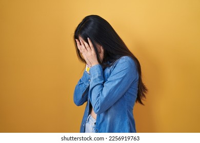 Young asian woman standing over yellow background with sad expression covering face with hands while crying. depression concept.  - Powered by Shutterstock