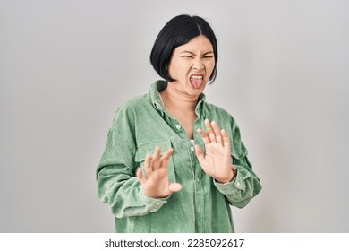 Young asian woman standing over white background disgusted expression, displeased and fearful doing disgust face because aversion reaction. 