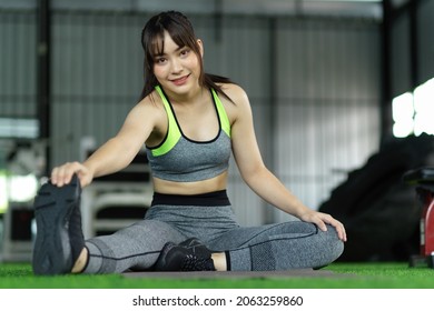 Young Asian Woman Stretching With A Hand To One Leg, Cool Down After Exercise Workout At Gym.