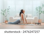 Young Asian woman stretching yoga workout on exercise mat while online training class with computer laptop in living room