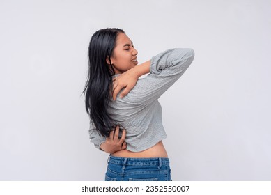 A young asian woman struggles to reach her back. A futile attempt to scratch her back with her own hands, the acnestis.