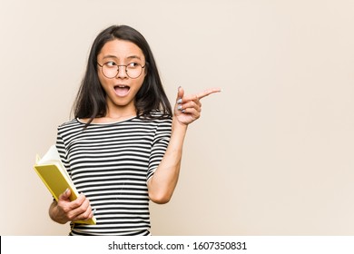 Young Asian Woman Student Holding A Book Pointing To The Side