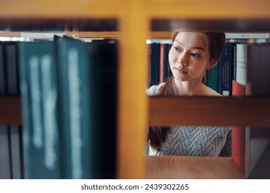 Young Asian woman student reaching for book on bookshelf in library. - Powered by Shutterstock