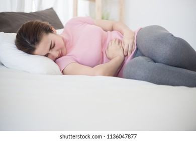 Young asian woman suffering from abdominal pain on the bed.