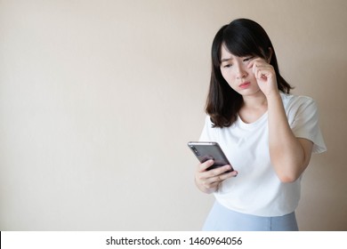 Young Asian Woman Suffering From Eye Strain Fatigue, Blurry Vision And Dry Eyes Symtoms While Using Mobile Phone. Smartphone Overuse And Eye Health Risks Concept. Copy Space.