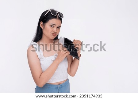 A young asian woman sulks and pouts revealing an empty wallet with no money. Isolated on a white background.