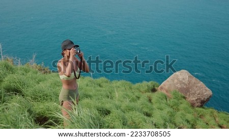 Young asian woman in summer clothes standing using camera to capture the beautiful scenery landscapes of the tropical island seas. A female traveler captures her travel memories with photographs.