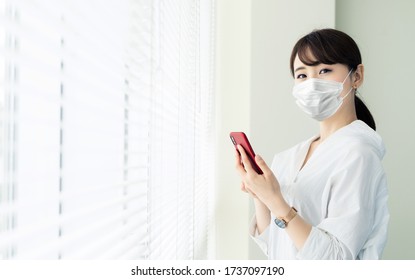 Young asian woman with surgical mask. Smart phone. - Powered by Shutterstock