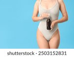 Young Asian woman in swimsuit with bottle of cocktail on blue background