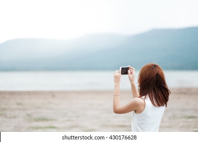 Young Asian woman taking photo with smart phone of landscape
