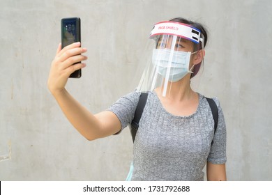 Young Asian Woman Taking Selfie With Mask And Face Shield For Protection From Corona Virus Outbreak Outdoors