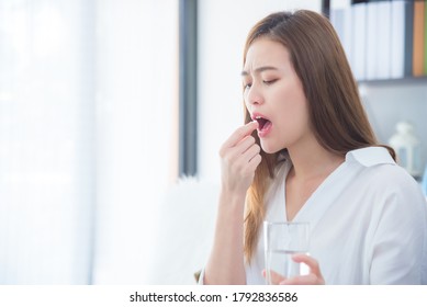 Young Asian Woman Taking A Tablet Of Painkiller Medicine And Feeling Pain Expression On Her Face .