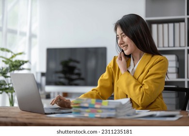 young asian woman talking on the mobile phone and smiling while sitting at her working place in office. - Shutterstock ID 2311235181
