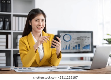 young asian woman talking on the mobile phone and smiling while sitting at her working place in office. - Shutterstock ID 2311235187
