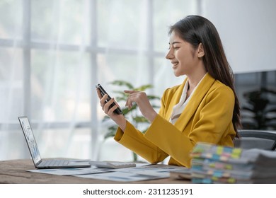 young asian woman talking on the mobile phone and smiling while sitting at her working place in office. - Shutterstock ID 2311235191