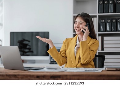 young asian woman talking on the mobile phone and smiling while sitting at her working place in office. - Shutterstock ID 2311235193