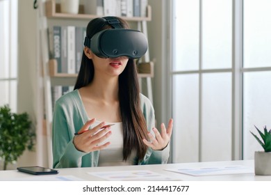 Young Asian Woman Talking While Using 360 VR Headset For Online Meeting In Metaverse At Home 